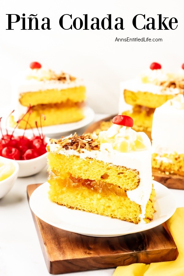 A pina colada cake cut open to show the filling and cake inside sit in the back left, a cut piece of cake sits on aa white plate front and center. There is a second piece in the upper left. A bowl of cherries sits between the two pieces of cake.