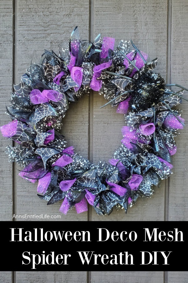 a purple and black Halloween wreath accented with spider ribbon and faux sider, hanging against a grey wall