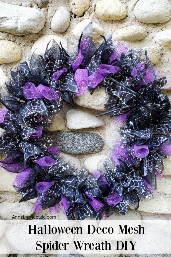 a purple and black Halloween wreath accented with spider ribbon and faux sider, hanging against a fireplacewall
