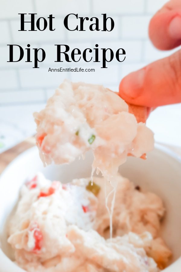 A scoop of crab dip on a cracker being lifted from a portion in the white bowl below