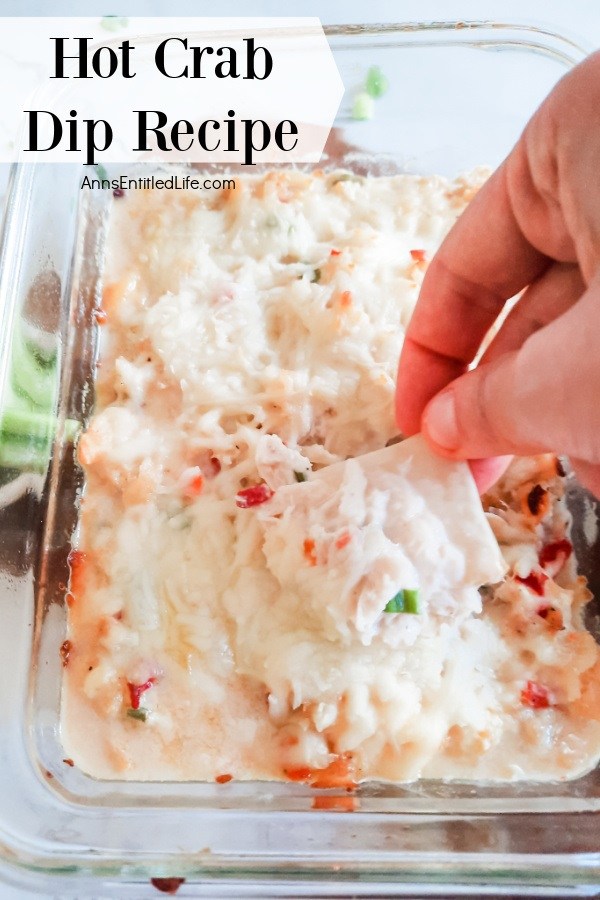 A a scoop of crab dip on a pita being lifted from the clear baking dish below, there are celery sticks to the left.