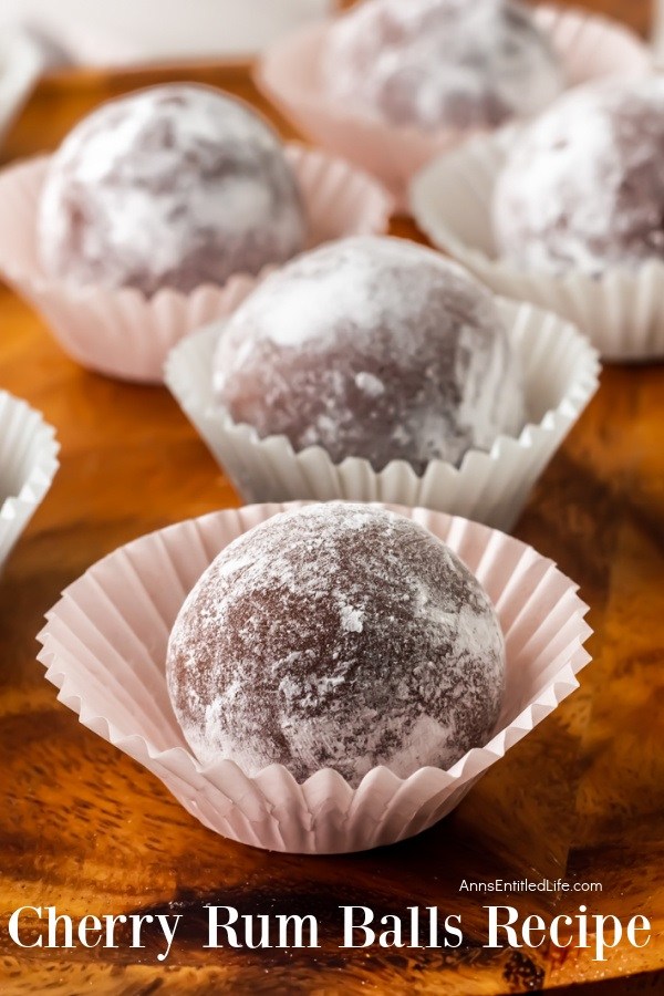 close-up of five cherry rum balls in a white candy wrapper sitting on a wooden board.