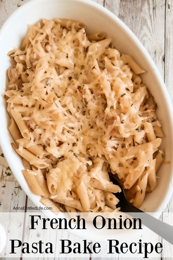 A white bowl filled with French onion pasta bake sits on a board, there is a black serving spoon in the dish