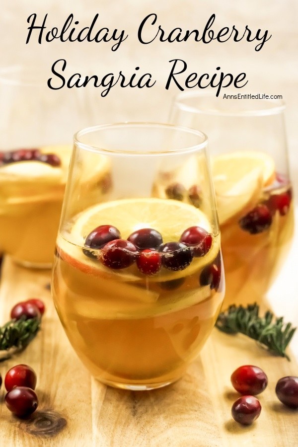 Holiday Cranberry Sangria Recipe Up close image of three glasses half-filled with holiday cranberry sangria and garnished with orange slices and cranberries sitting on a wooden board. There are cranberry and rosemary garnishes sitting on the board as decorations
