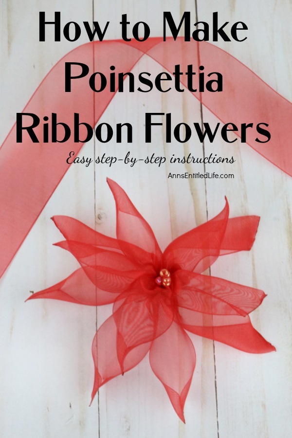 One red poinsettia ribbon flower sits on a beach plank background. There is a length of red ribbon at the top.