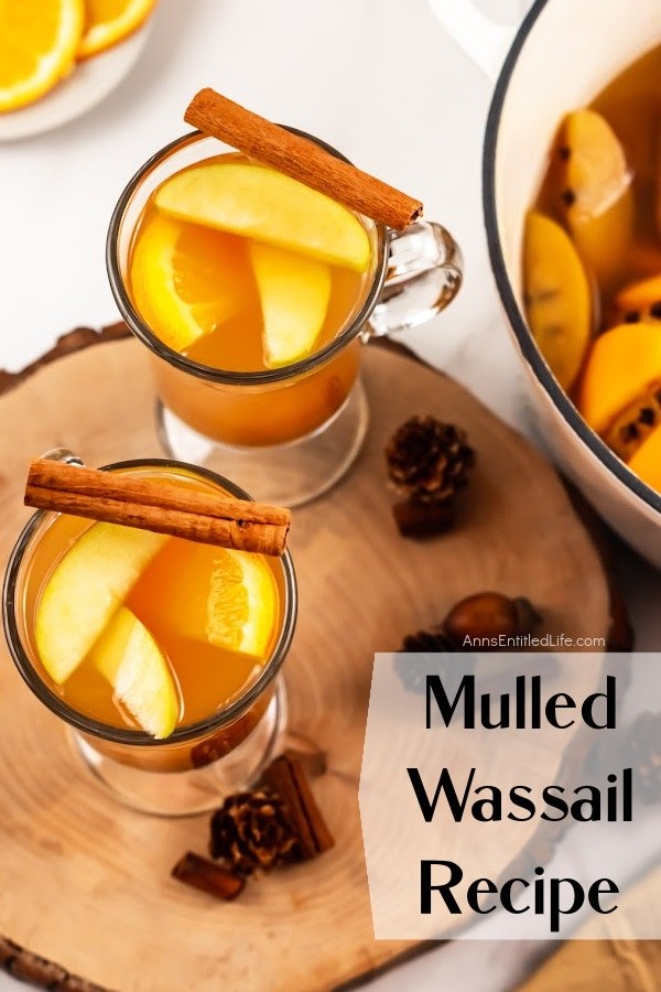 An overhead view of two mugs filled with mulled wassail sitting on a wooden board, the remaining stockpot is on the right.