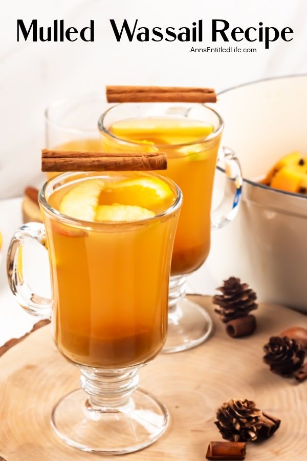 A side view of two mugs filled with mulled wassail sitting on a wooden board, the remaining stockpot is on the right.