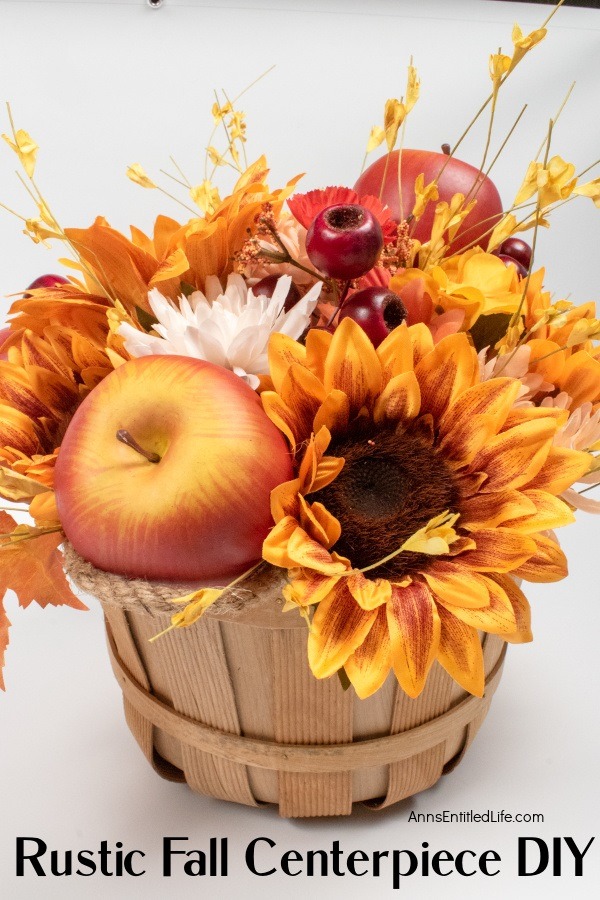 A small bushel basket filled with autumn flowers, leaves, berries, and apples in a short floral arrangement