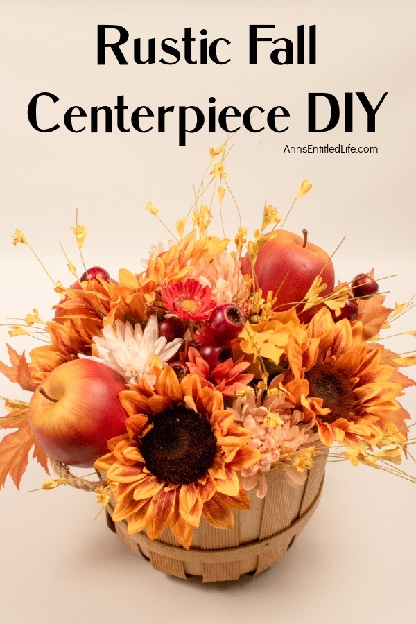 A small bushel basket filled with autumn flowers, leaves, berries, and apples in a short floral arrangement