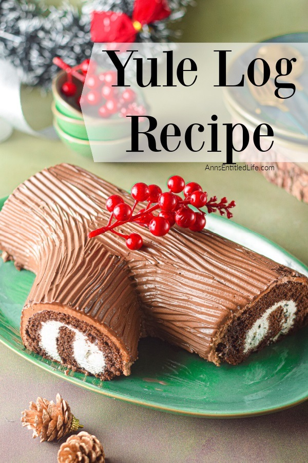 A yule log cake on a green platter with faux cranberries adorning it, there are holiday decorations in the upper part of the photo