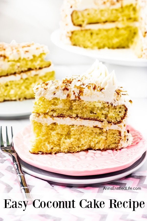 A piece of coconut cake sits on a pink serving dish, there is a fork to the left. A second piece is in the upper left. The remaining cake is on a white cake plate in the upper right. All this sits on a pink and grey chevron napkin.