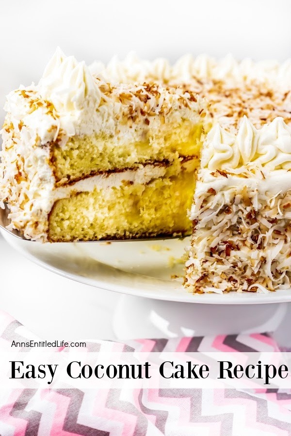 A piece of coconut cake trimmed with ruffle mounds and decorated with toasted coconut on a white cake plate, one piece is being lifted from the cake.
