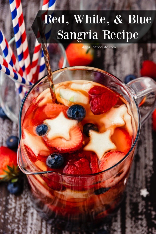Overhead view of a pitcher of red, white, and blue sangria is a clear pitcher. There are red and white and blue and white straws in a glass to the right.