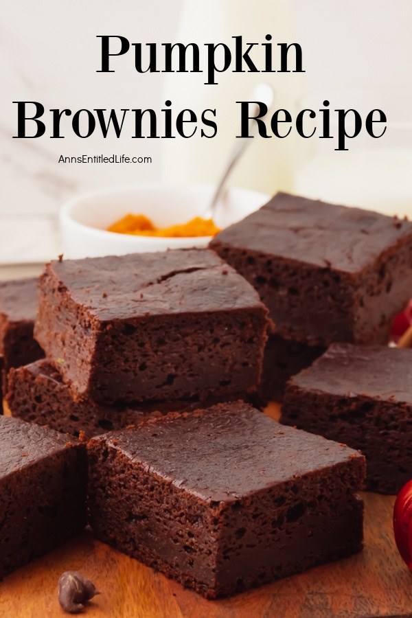 A stack of cut pumpkin brownies on a wooden cutting board, a white bowl of pumpkin puree is in the upper center in back