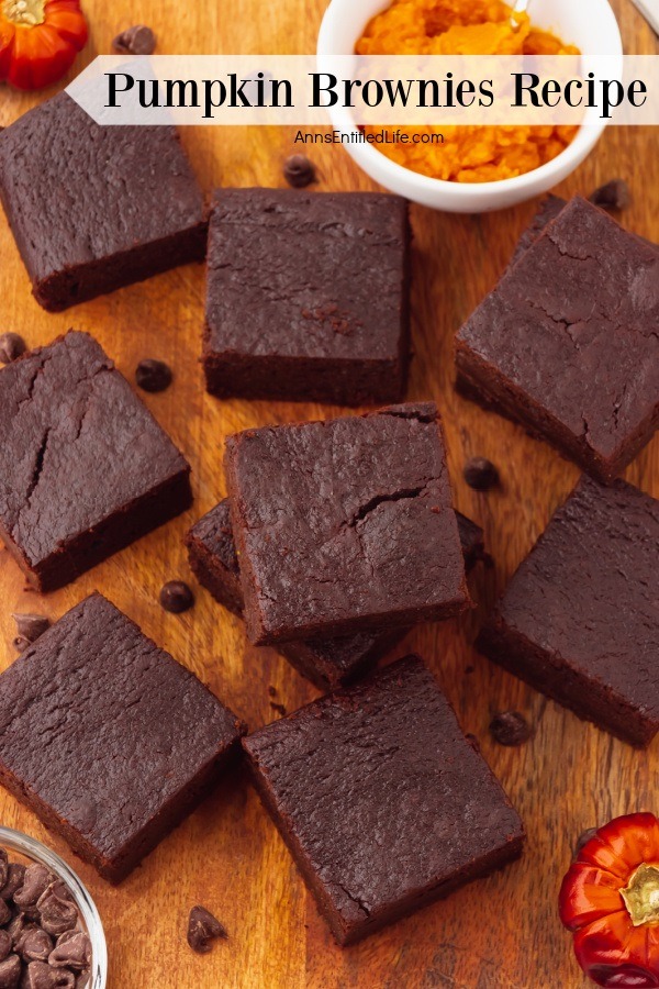 An overhead view of  cut pumpkin brownies on a wooden cutting board, a white bowl of pumpkin puree is in the upper right, a bowl of chocolate chips is in the lower left