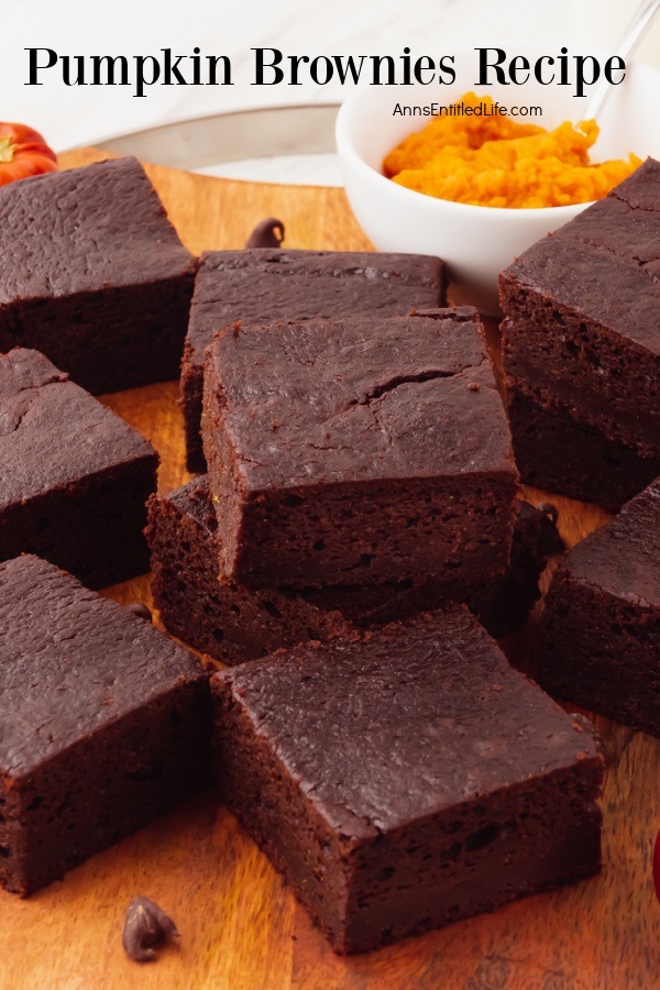 A stack of cut pumpkin brownies on a wooden cutting board, a white bowl of pumpkin puree is in the upper right