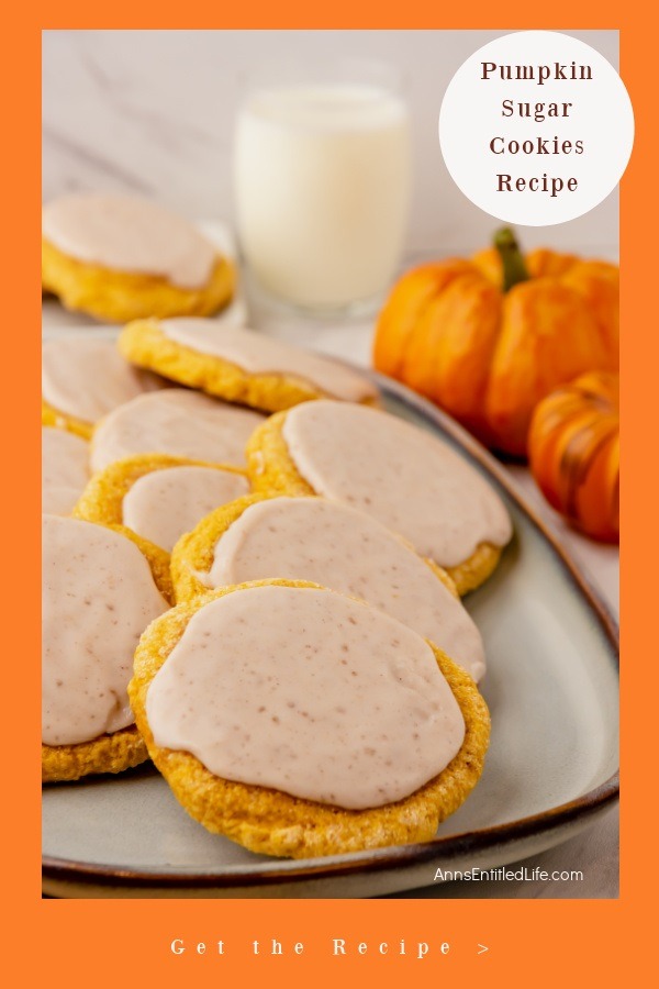 A white platter filled with pumpkin sugar cookies, a glass of milk in the upper center, some decorative pumpkins in the upper right