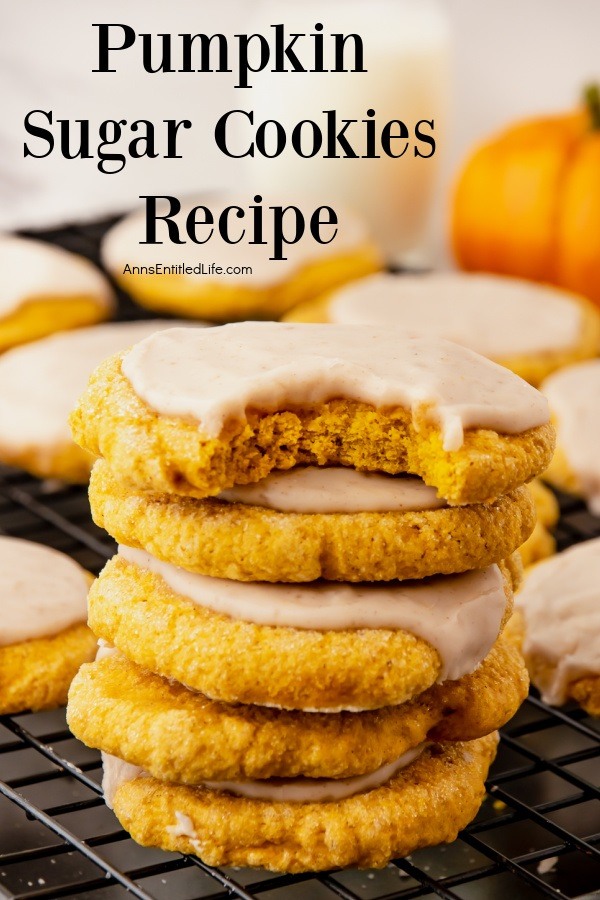A stack of pumpkin sugar cookies sitting on a baking wire rack, the top cookie is missing a bite