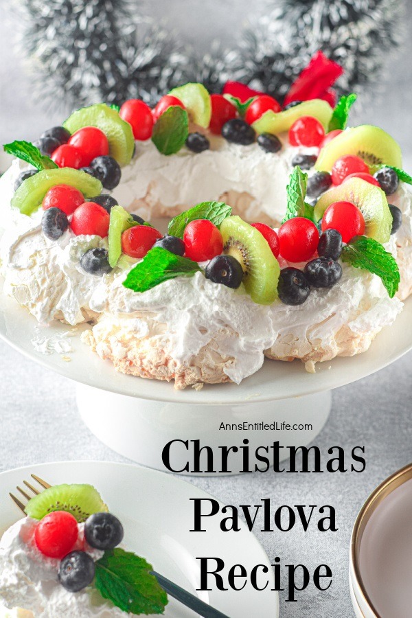 Christmas pavlova wreath on a white cake stand with a slice on a white plate in the lower left.