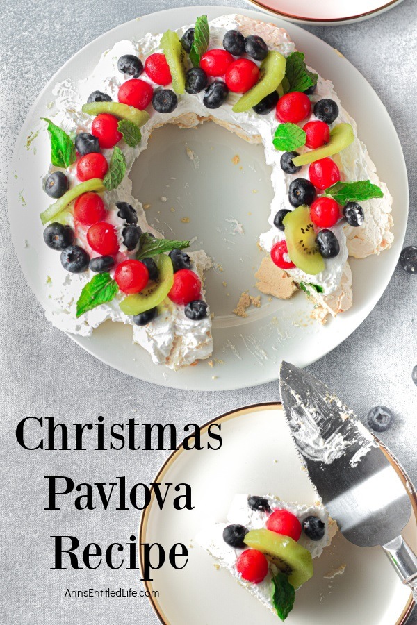 Overhead view of a Christmas pavlova wreath on a white cake stand with a slice on a white plate in the lower right.