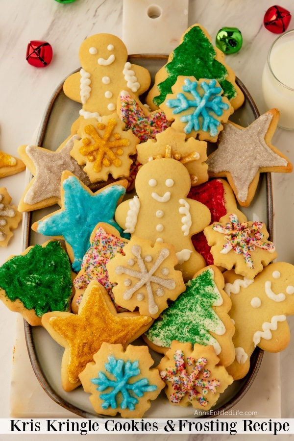 A white plate filled with frosted and decorated Kris Kringle cookies, holiday decor surrounds the plate