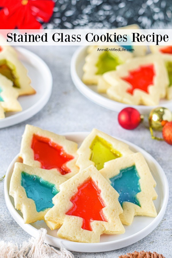 Three white plates are filled with stained glass cookies. There are small Christmas tree bulb decorates in between the plates.