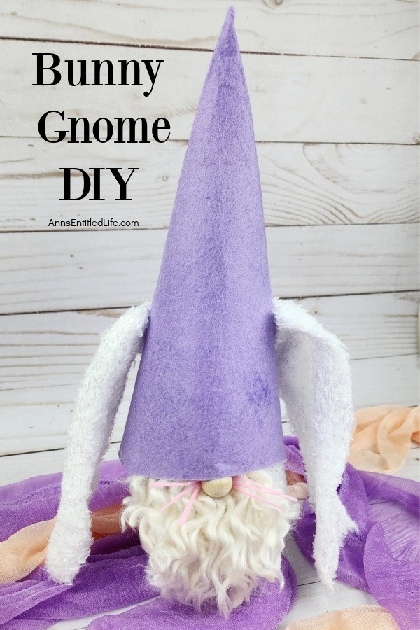 a homemade bunny gnome against a grey background, sitting on orange and purple scarves