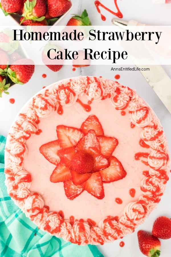 An overhead view of a whole, decorated homemade strawberry cake on a white background. There are fresh strawberries in the upper left and center.