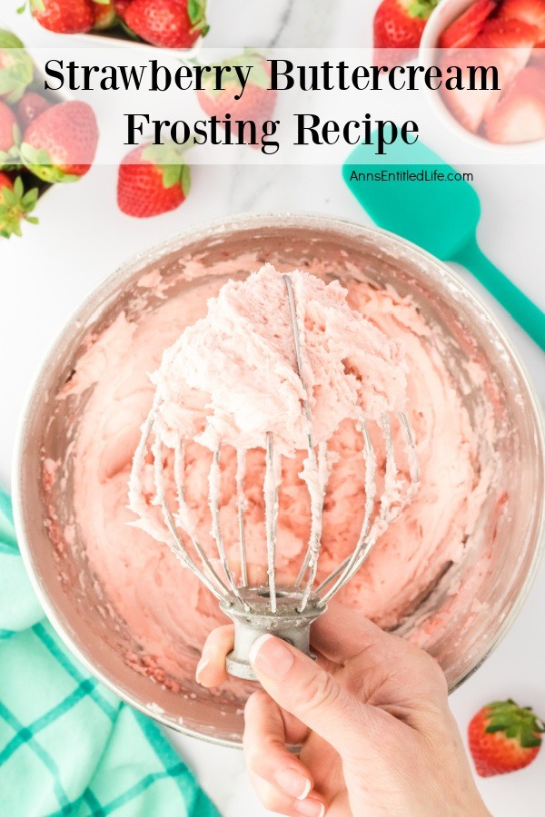An overhead view of a woman's hand holding an electric mixer whisk filled with strawberry frosting. The mixing bowl filled with strawberry frosting is underneath the whisk.