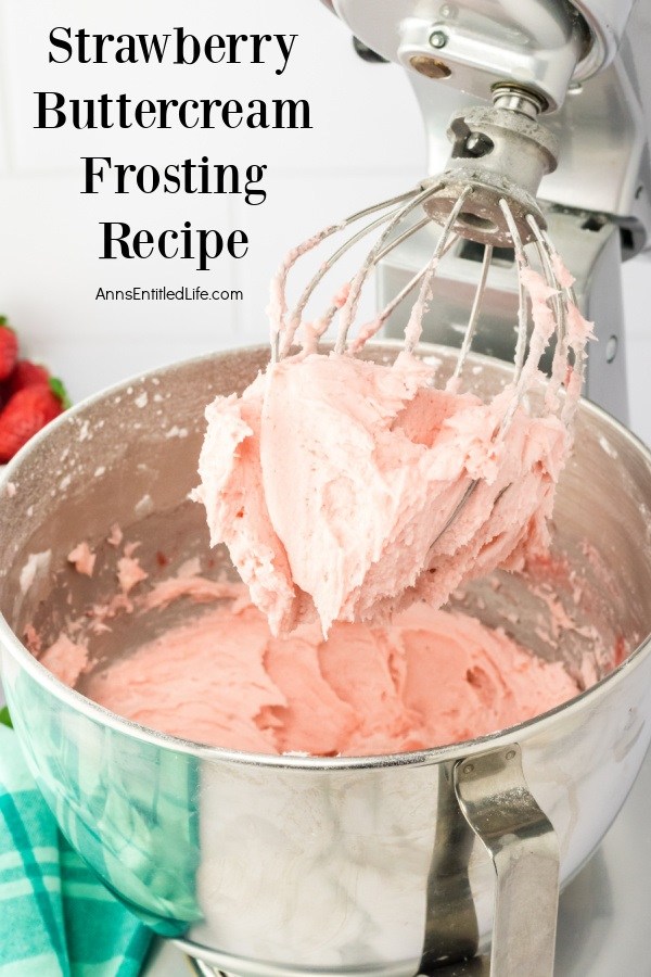 A photo of a stand mixer and mixing bowl filled with strawberry frosting, the whisk is raised and covered with strawberry frosting