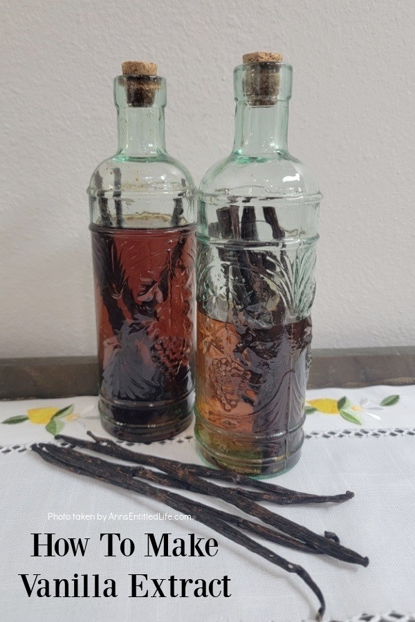 Two bottles of aged vanilla extract on a white place mat. There are five vanilla beans in front of the bottles