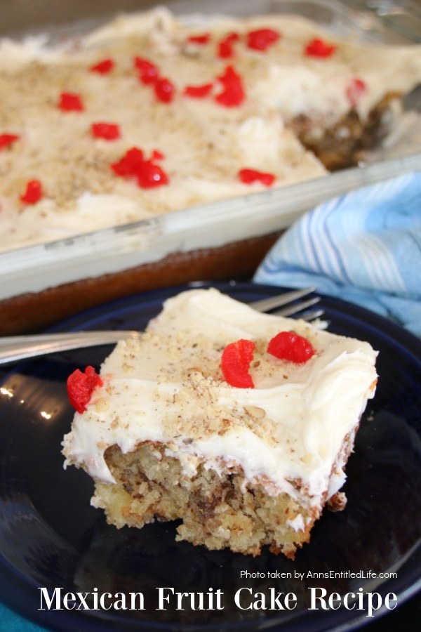 A piece of Mexican fruit cake on a blue plate is front and center, the remaining cake is in the upper portion of the photo in a clear pan