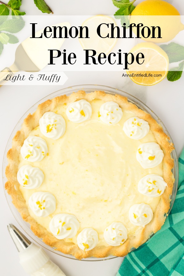 A whole lemon chiffon pie sits on a white counter. There is a checked green napkin in the lower right, a whipped cream pastry bag in the lower left, a cut lemon in the upper right, and a pie server in the upper left.