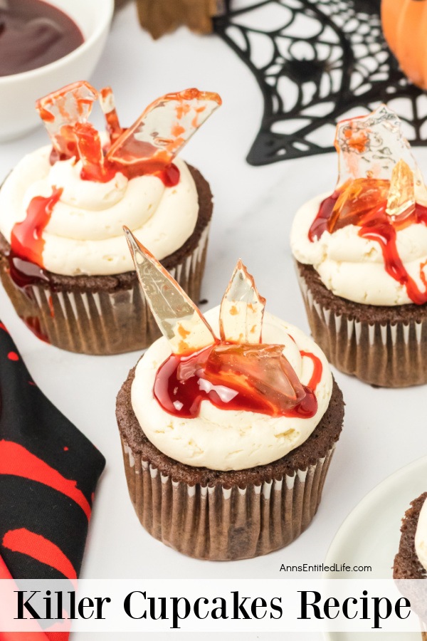 side view of killer cupcakes on a white surface, halloween decorations in the upper right, a bowl of melted chocolate in the upper left
