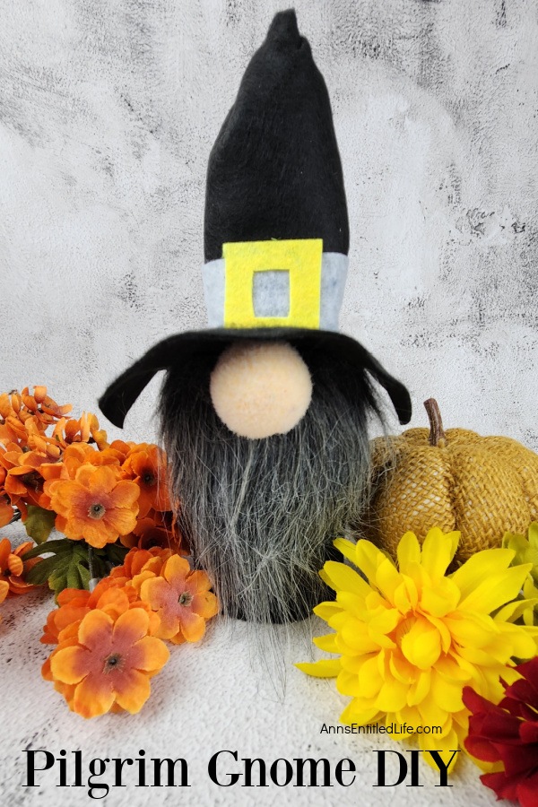 Homemade gnome pilgrim surrounded by faux autumn flowers and pumpkin