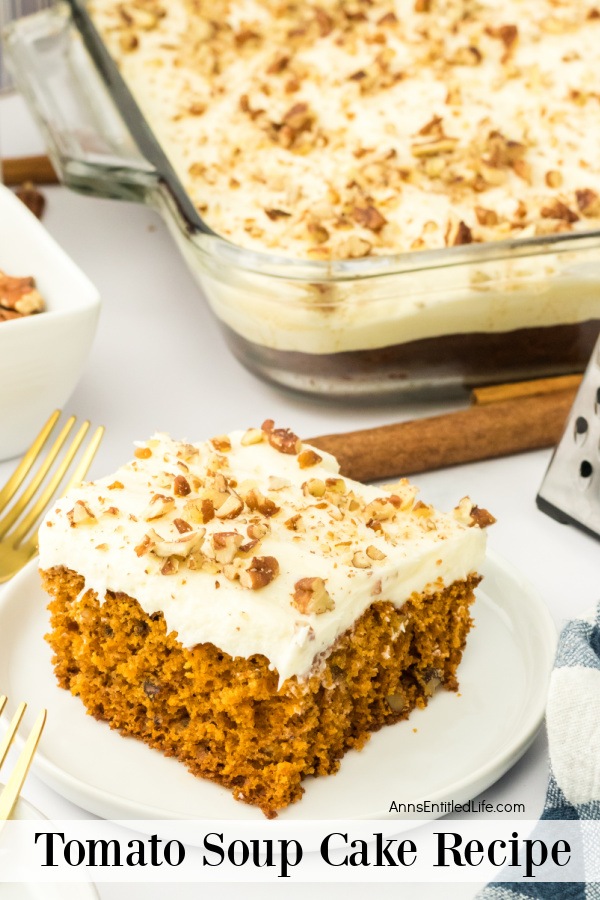 A piece of tomato soup cake is on a white plate at the forefront. The rest of the cake pan is in the upper right. A gold fork is to the left of the plate, a white bowl of nuts is above the fork.