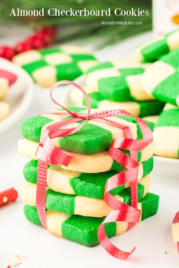 A stack of 5 checkerboard cookies tied with a red ribbob. There are red and green checkerboard cookies in the background.