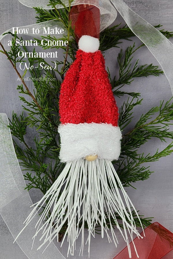 Homemade Santa gnome ornament set on top of pine and white ribbon against a grey background