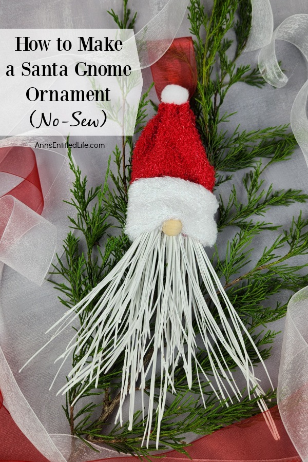 Homemade Santa gnome ornament set on top of pine and white ribbon against a grey background