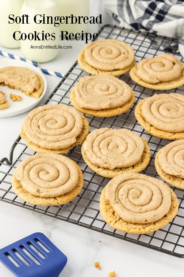 Wire rack filled with frosted soft gingerbread cookies, a blue spatula in front of it, a cookie on a white plate is in the upper left