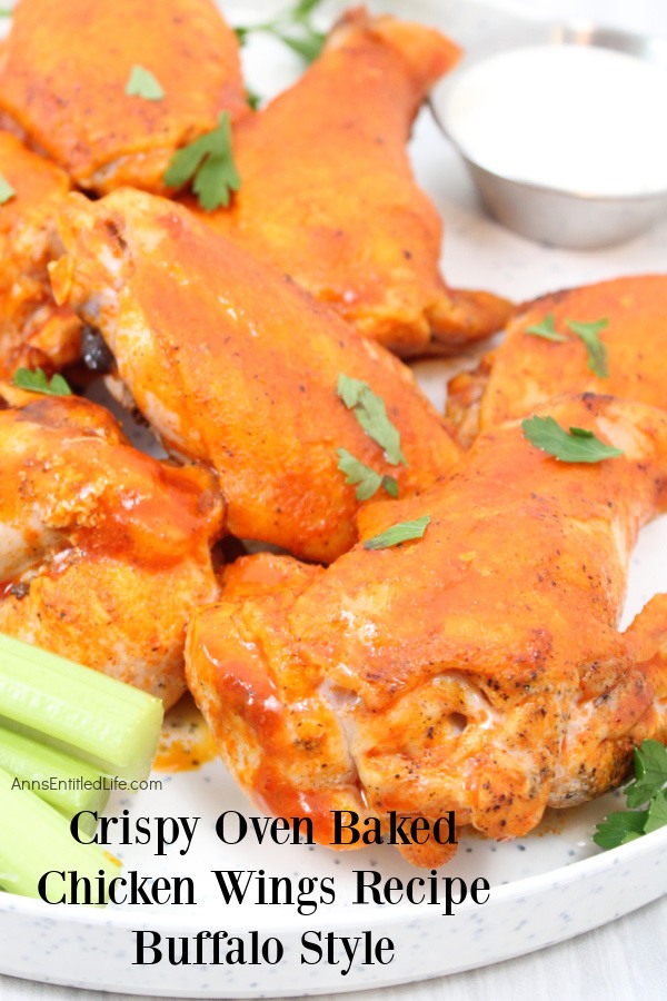 a pile of baked chicken wings on a white plate, a small servings bowl of bleu cheese on the right side, celery sticks in the lower left