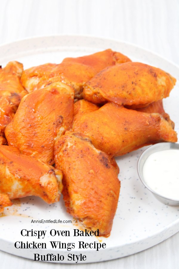a pile of baked chicken wings on a white plate, a small servings bowl of bleu cheese on the right side