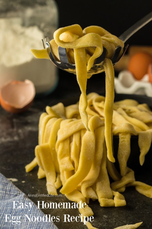 A spoonful of homemade egg noodles being lifted from a bowl of homemade egg noodles. There are eggs in the upper right, flour in the upper left.