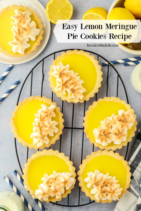 An overhead view of a five lemon meringue pie cookies on a wire rack, a sixth cookie is in the upper left, a bowl of lemons in the upper right