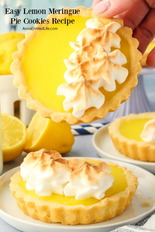 A lemon meringue pie cookie sits on a white plate, there is another cookie being held front forward above it