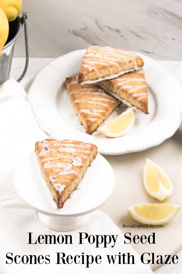 A lemon poppy seed scone sits on a white plate, a stack of three other scones sits on another white plate in the upper right. A bucket of lemons are barely seen in the upper left.