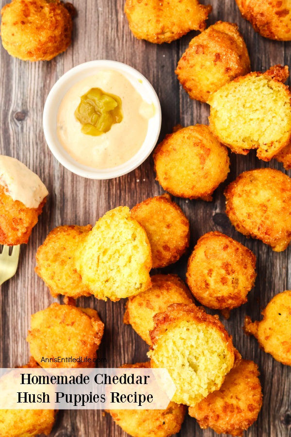 Cheddar hush puppies on a wooden platter surrounding a white bowl filled with chili aioli 