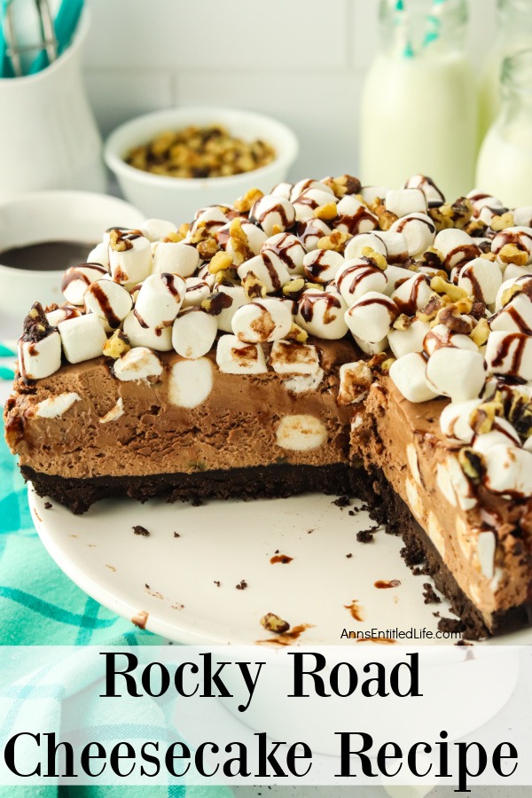 A front view no-bake rocky road cheesecake on a white cake plate with several pieces missing