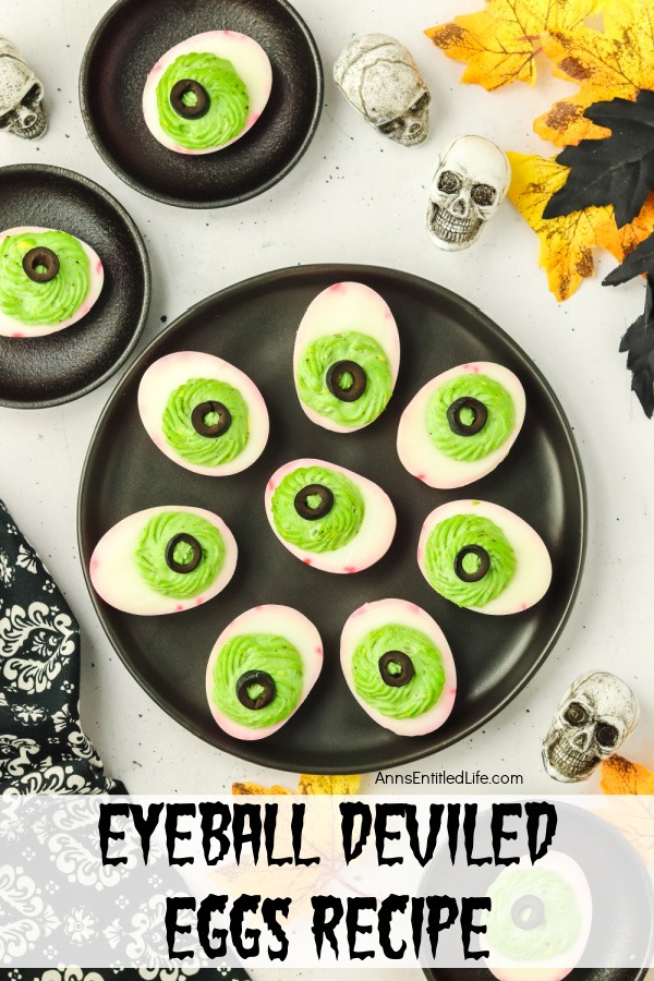 Eyeball Deviled Eggs Recipe for Creepy Halloween Snacks Ovehead view of a black plate filled with deviled eggs made to look like red veined eyeballs, there are two smaller plates with a single deviled egg in the upper left. Halloween skull decor surround the plate.