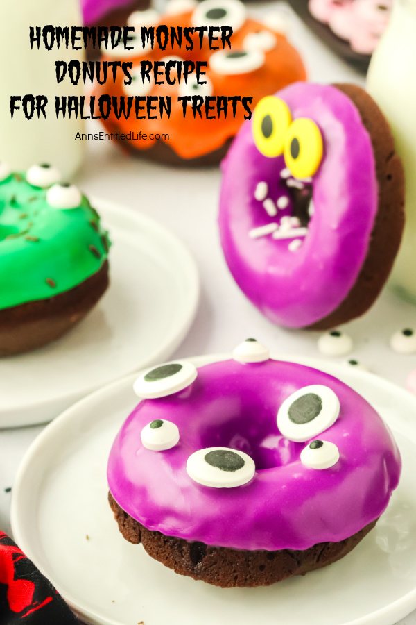 Close-up view of a chocolate donuts with purple glaze and colorful eyes on a white plate, there are there similarly decorated donuts behind it